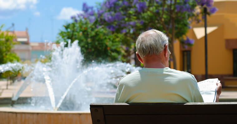 Old man sitting on a bench reading a newspaper Old man sitting on a bench reading a newspaper